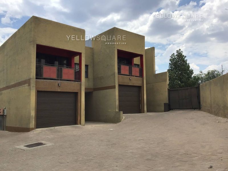 Front elevation of a townhouse complex featuring double garage doors, upper-level balconies, and a paved driveway with secure perimeter walling.