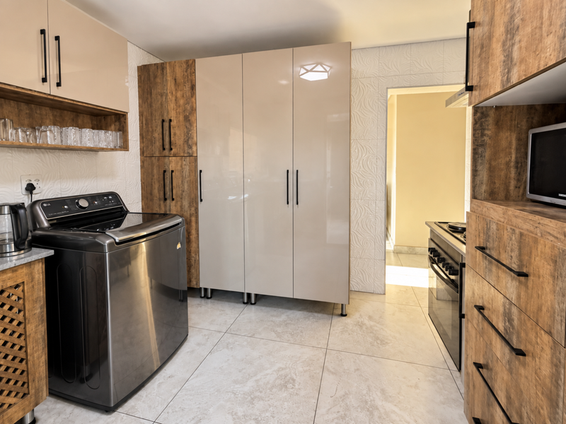 Modern scullery featuring high-gloss and wood-grain cabinetry, tiled flooring, textured wall finishes, and integrated appliances including an oven and microwave.