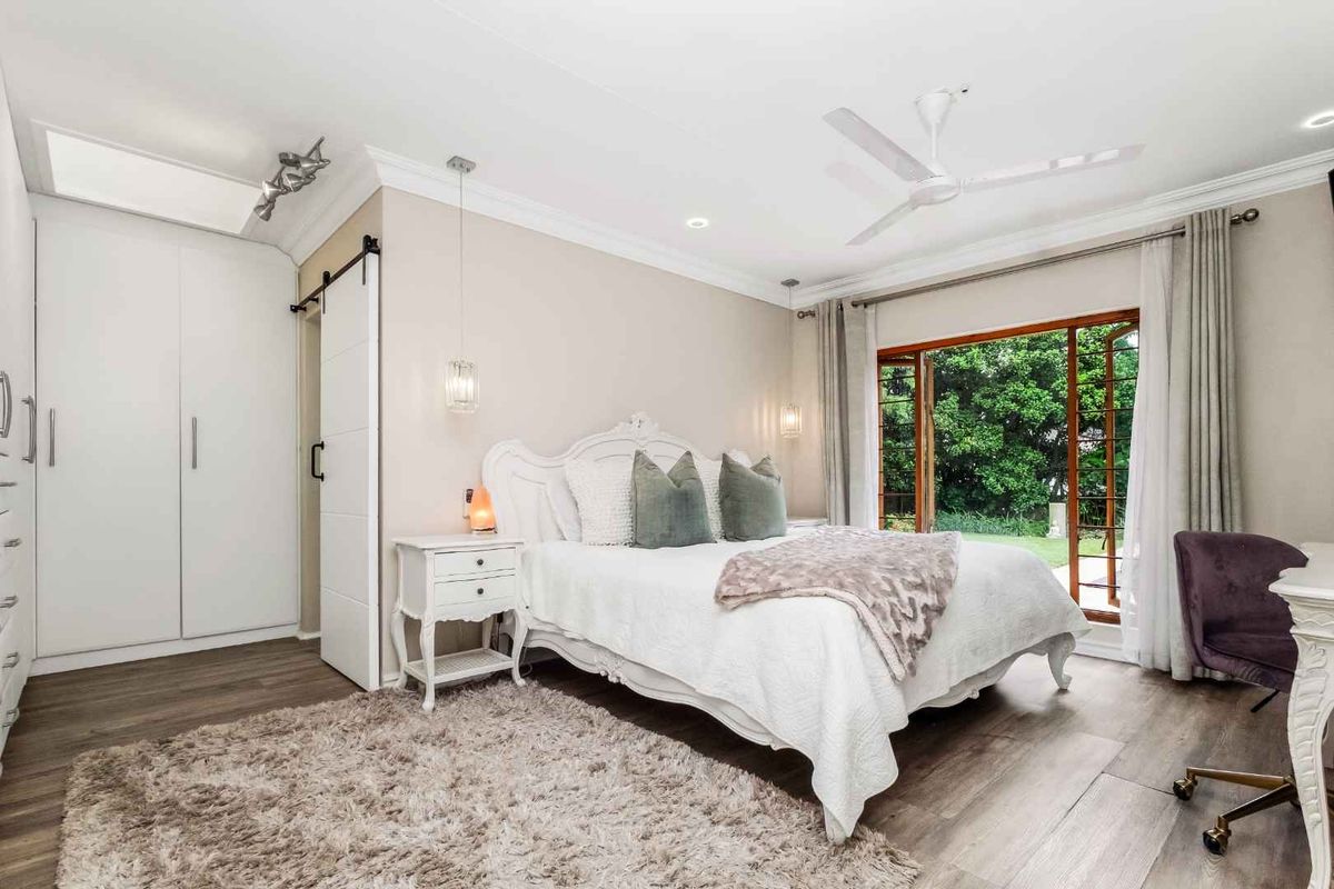 A bright and spacious bedroom featuring built-in wardrobes, a sliding barn door, modern ceiling fan, and direct access to the garden through wooden doors.