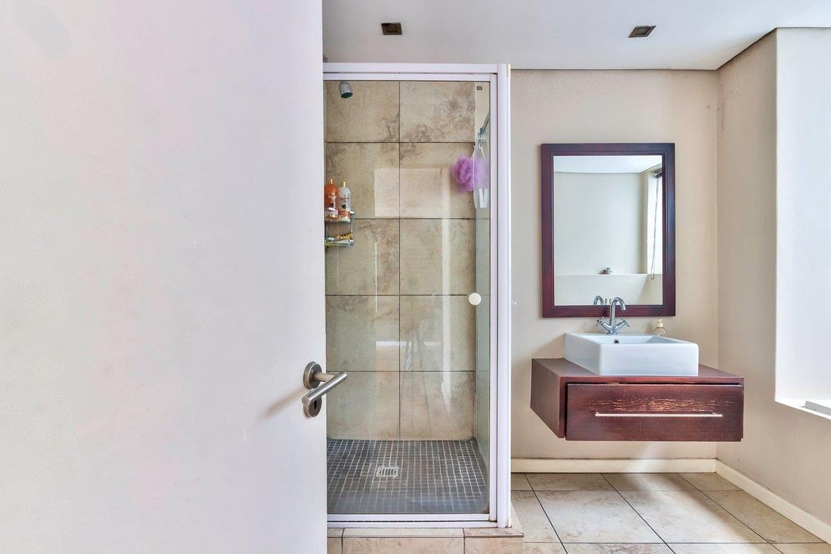 A functional bathroom featuring a glass-enclosed shower with tiled walls, a floating vanity with a vessel sink, and a wall-mounted mirror.