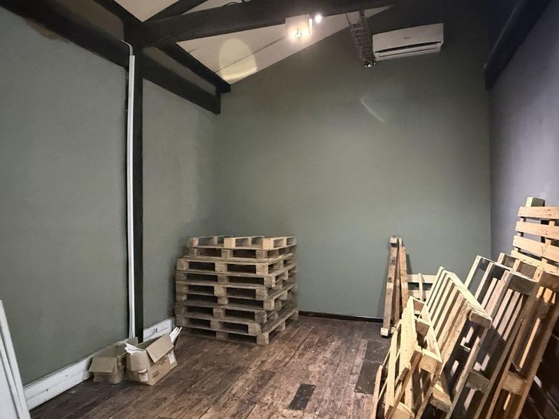 A functional office space featuring exposed timber beams, split-system air conditioning, and timber flooring, currently utilized as a storage area.