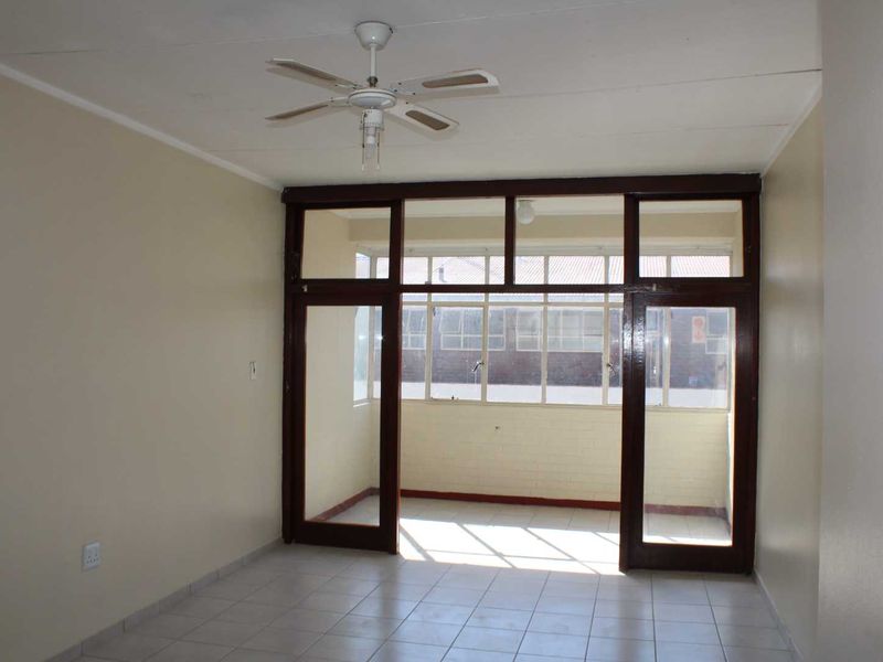 An empty living room featuring tiled flooring, a ceiling fan, and large timber-framed glass doors leading to an enclosed balcony area.