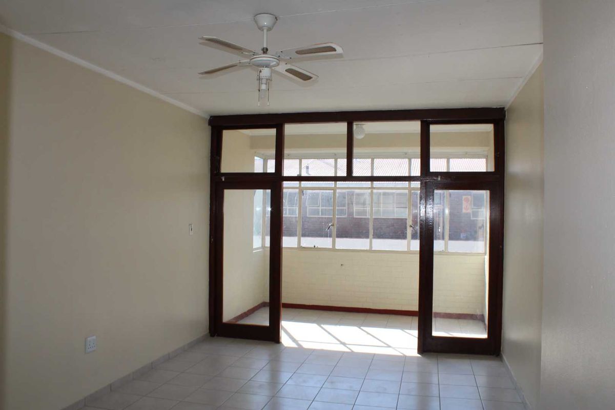 An empty living room featuring tiled flooring, a ceiling fan, and large timber-framed glass doors leading to an enclosed balcony area.