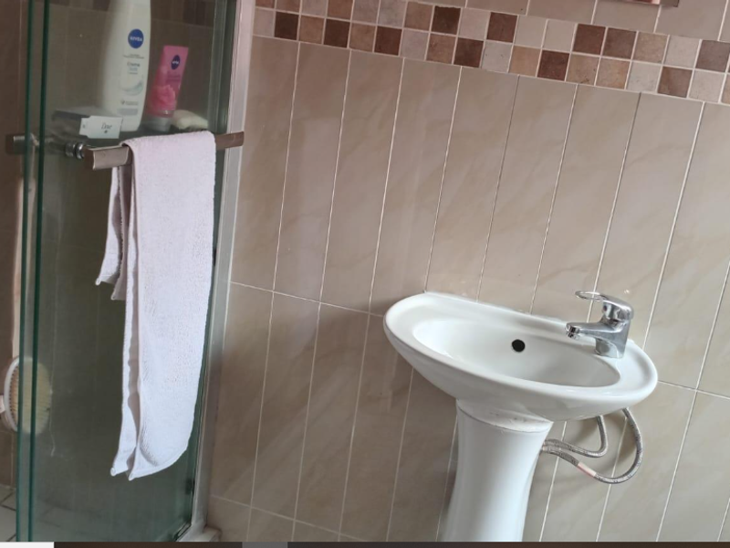 A functional bathroom featuring a pedestal basin with chrome mixer tap and a glass-enclosed shower with neutral ceramic wall tiling.