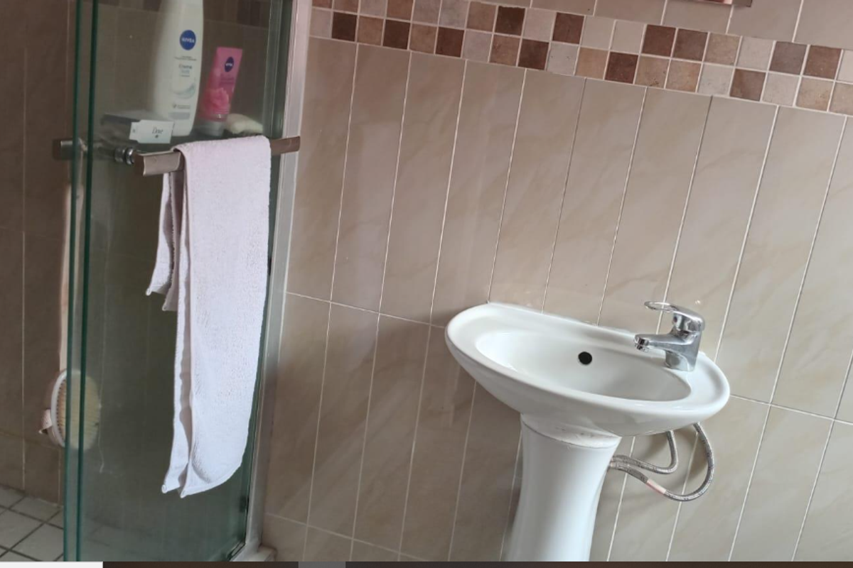 A functional bathroom featuring a pedestal basin with chrome mixer tap and a glass-enclosed shower with neutral ceramic wall tiling.
