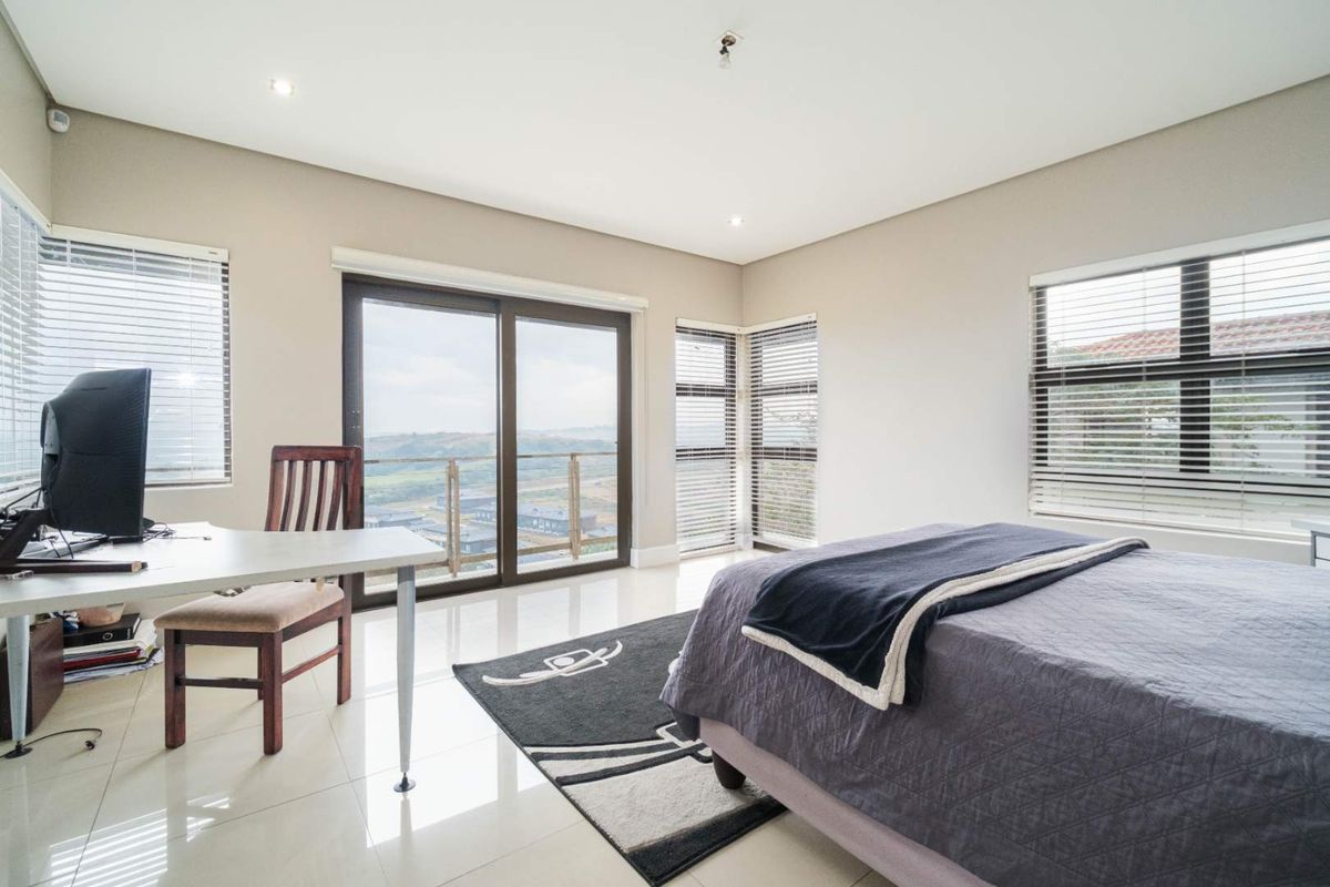 Spacious bedroom featuring large windows, tiled flooring, and sliding glass doors leading to a balcony with scenic views.