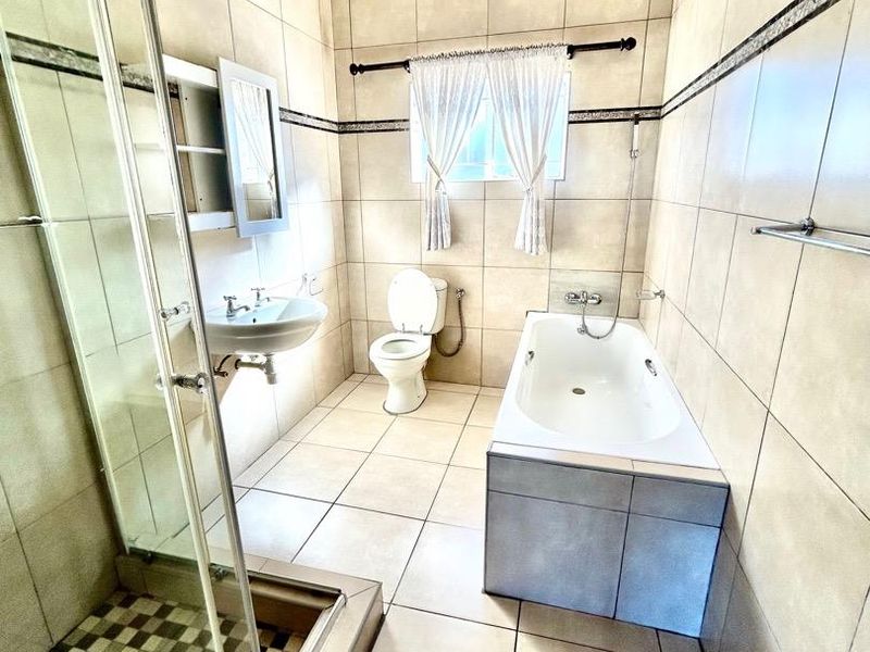 A spacious bathroom featuring a glass shower enclosure, a built-in bathtub, a wall-mounted basin, and a toilet, finished with neutral floor-to-ceiling wall tiles.
