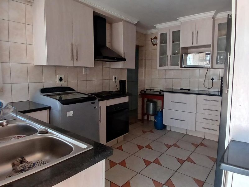 Functional kitchen featuring built-in cabinetry, double basin sink, integrated oven, extractor fan, and tiled finishes throughout.