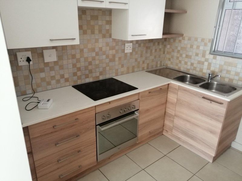 A clean and functional kitchen featuring light wood-finish cabinetry, mosaic tile backsplash, built-in oven and hob, and a stainless steel double sink.