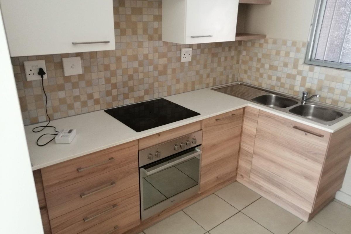 A clean and functional kitchen featuring light wood-finish cabinetry, mosaic tile backsplash, built-in oven and hob, and a stainless steel double sink.