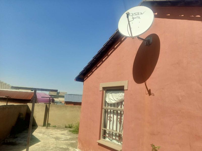 Rear exterior view of the property featuring a concrete paved yard, boundary wall, and a satellite dish mounted on the exterior wall.