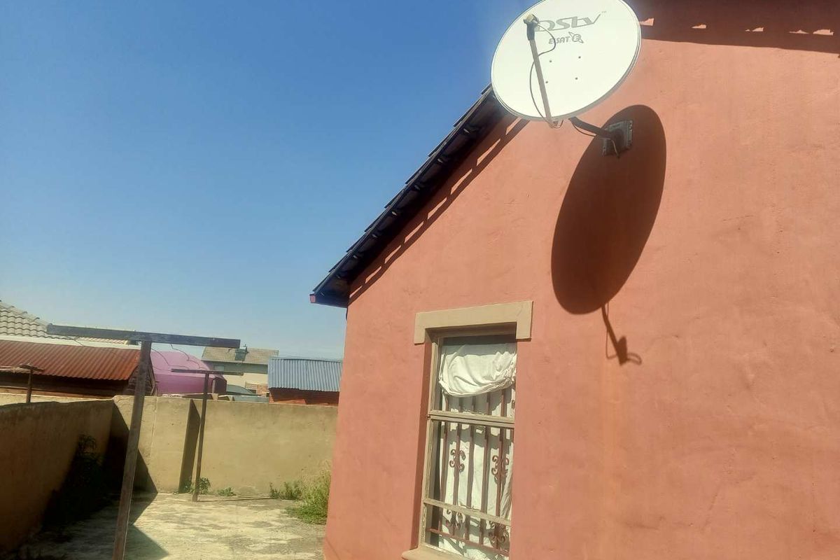 Rear exterior view of the property featuring a concrete paved yard, boundary wall, and a satellite dish mounted on the exterior wall.