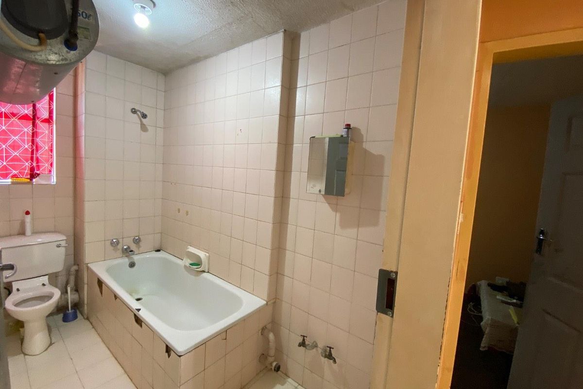 A dated bathroom featuring a standard bathtub, toilet, and wall-to-floor tiling, requiring modernization of fixtures and finishes.