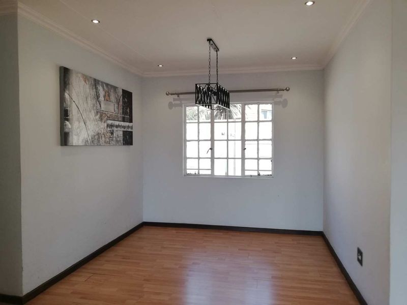 A bright, empty living room featuring laminate flooring, recessed downlighting, and a central pendant light fixture.
