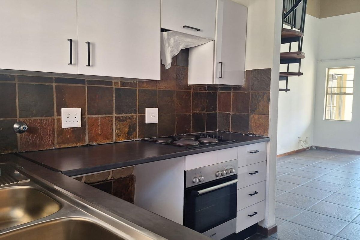 A functional kitchen featuring white cabinetry, dark countertops, a built-in oven and hob, and a tiled backsplash, adjacent to an open-plan living area.