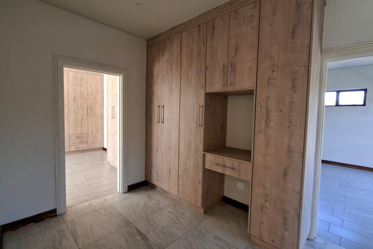 A spacious bedroom featuring extensive built-in wooden cabinetry with integrated vanity or desk space, tiled flooring, and neutral finishes.