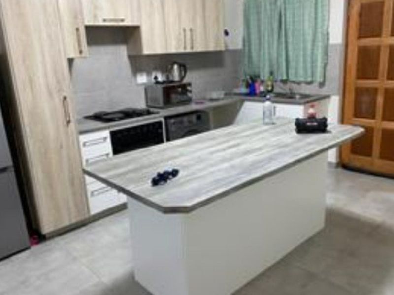 A functional kitchen featuring light wood-tone cabinetry, a central island with a laminate countertop, built-in oven, hob, and tiled flooring.