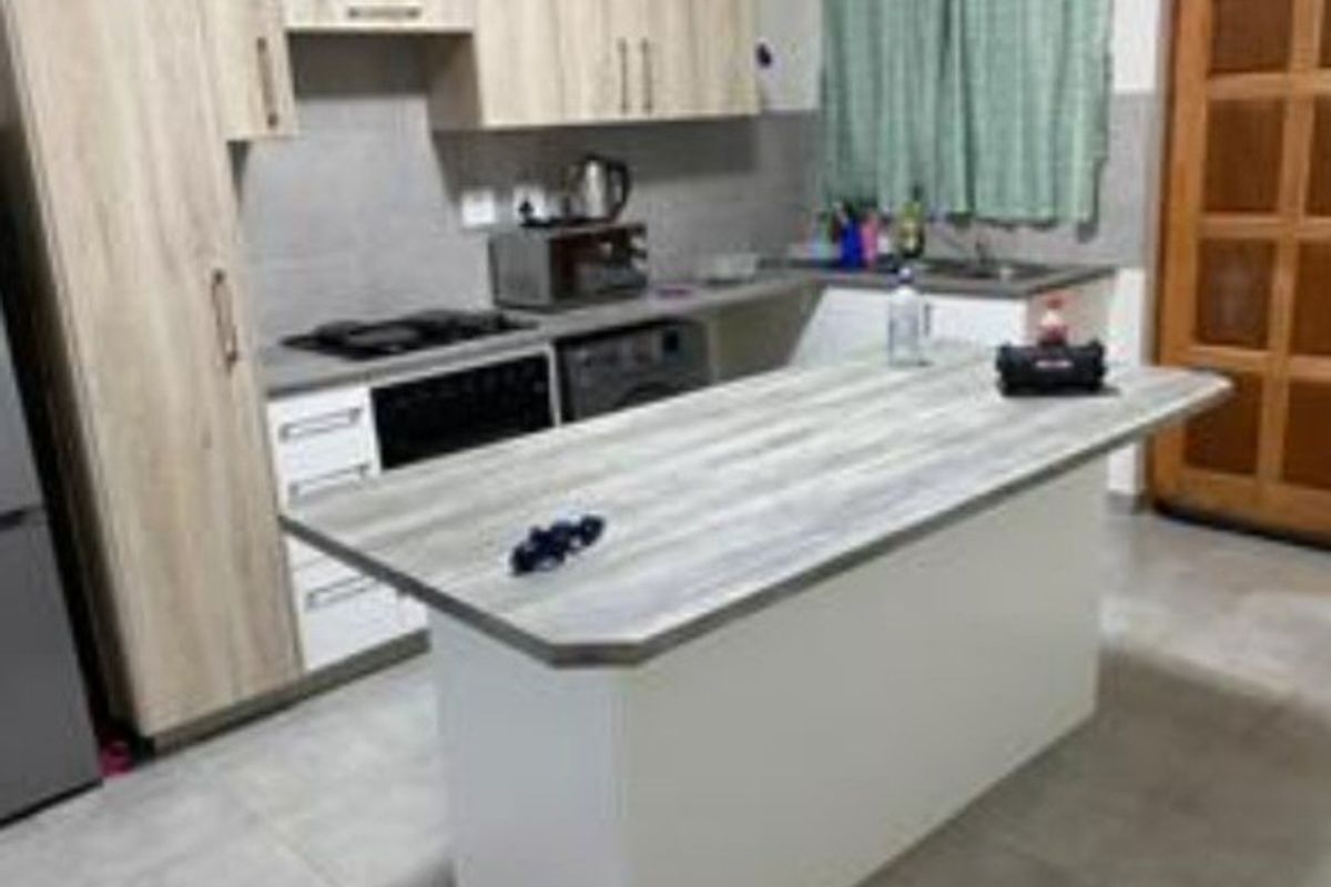A functional kitchen featuring light wood-tone cabinetry, a central island with a laminate countertop, built-in oven, hob, and tiled flooring.
