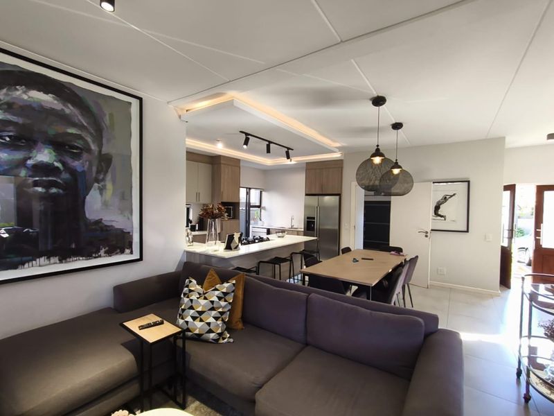 Modern open-plan living and kitchen area featuring a central island, sleek cabinetry, recessed lighting, and neutral tiled flooring throughout.