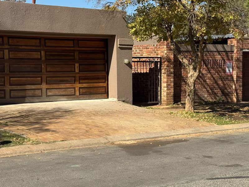 Front view of the property featuring a double garage with wooden doors, a paved driveway, and a brick boundary wall with a pedestrian gate.