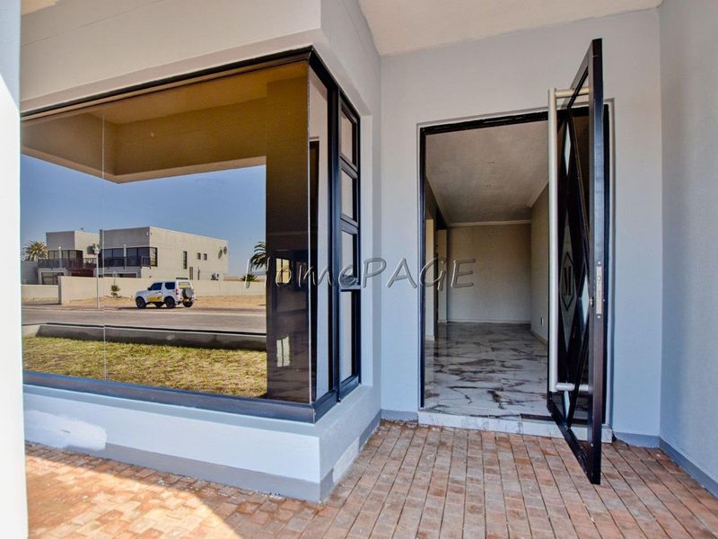 Modern entrance featuring a large pivot door, expansive glass window, and polished marble-look flooring leading into an open interior space.