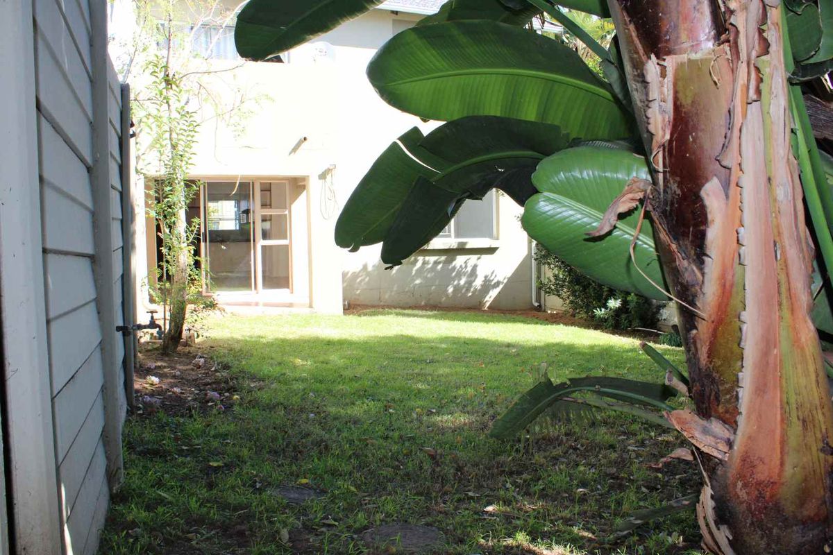 A view of the rear garden area featuring a small lawn, established plant life, and access to the building via sliding glass doors.