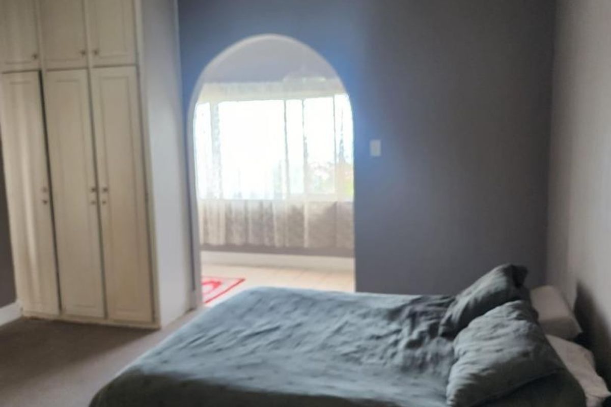 A bedroom featuring built-in cupboards, a ceiling fan, and an arched opening leading to an adjacent sunroom or balcony area.