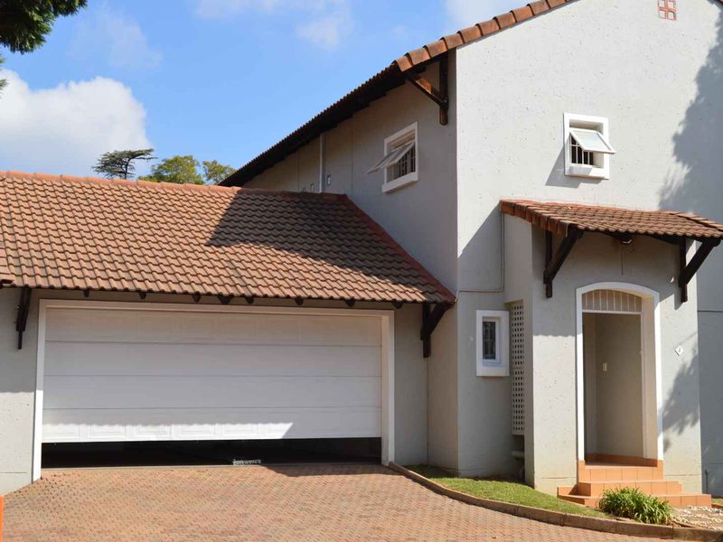 Front elevation of a residential property featuring a paved driveway, automated garage, and a covered entrance with tiled roof detailing.