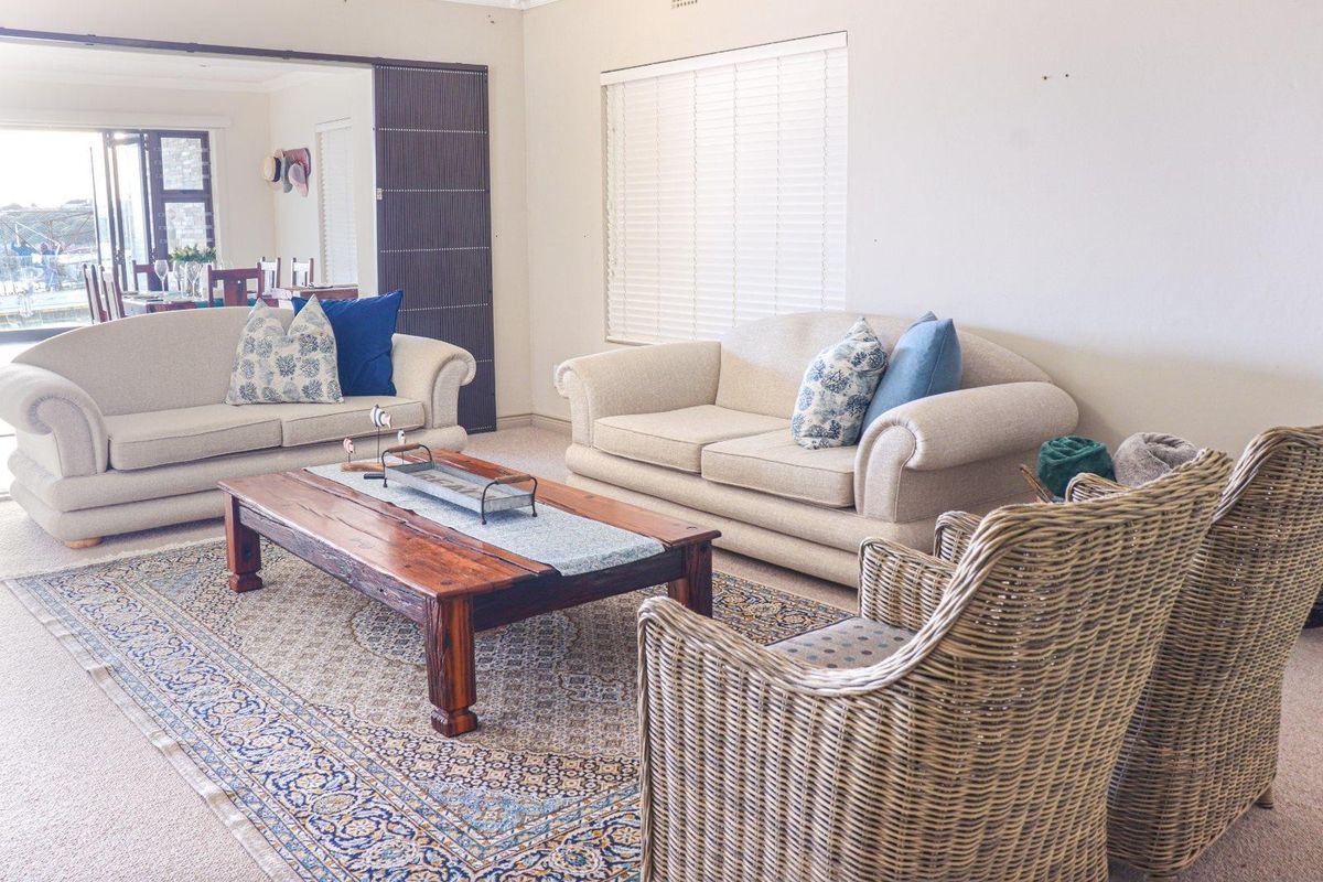 A spacious living room featuring neutral carpeting, large windows with fitted blinds, and an open-plan layout connecting to the adjacent dining area.