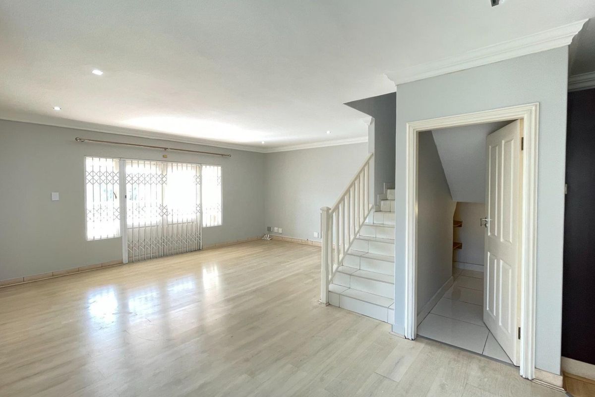 Spacious, light-filled living area featuring laminate flooring, a staircase with under-stair storage, and secure access to the exterior.