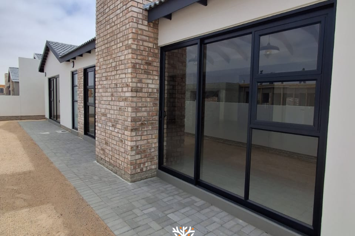 Rear exterior view of a townhouse featuring a brick chimney, paved walkway, and modern black-framed sliding glass doors.