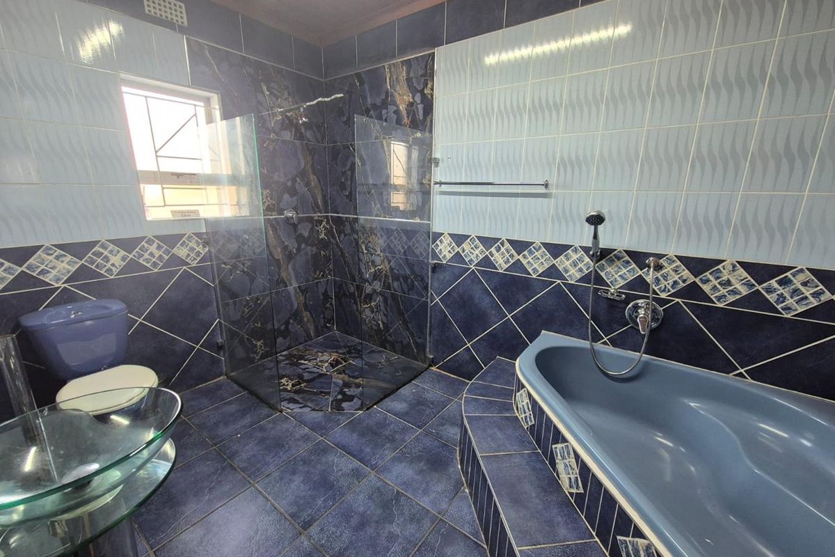 A spacious bathroom featuring a glass-enclosed shower, a built-in bathtub, and extensive blue-toned wall and floor tiling.