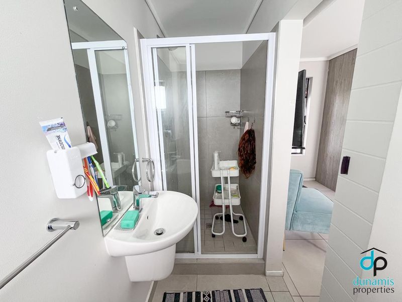 A compact, modern bathroom featuring a pedestal basin, a glass-enclosed shower, and neutral wall tiles.
