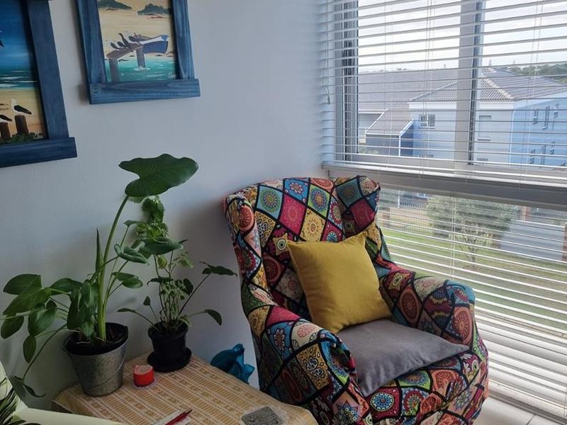 A cozy corner of a living area featuring tiled flooring and large windows fitted with venetian blinds, offering natural light and a neighborhood view.