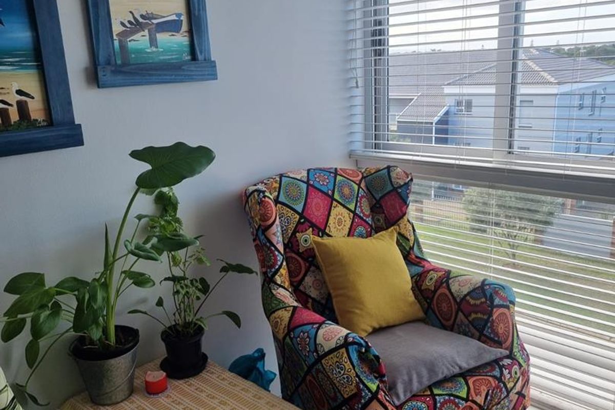 A cozy corner of a living area featuring tiled flooring and large windows fitted with venetian blinds, offering natural light and a neighborhood view.