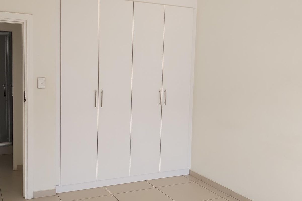A clean, empty bedroom featuring neutral tiled flooring and ample built-in cupboard storage, with direct access to an adjoining bathroom.
