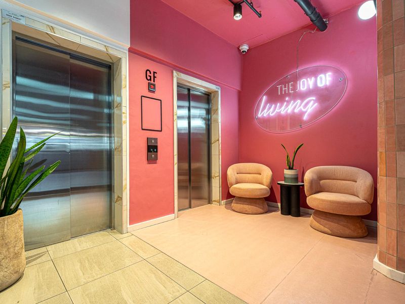 Modern apartment building lobby entrance featuring dual stainless steel elevators, vibrant pink accent walls, and contemporary tiled flooring.