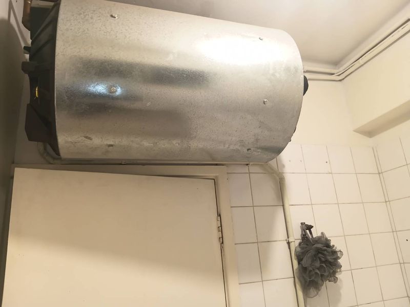 A bathroom interior featuring an exposed wall-mounted electric water heater and basic white wall tiling.