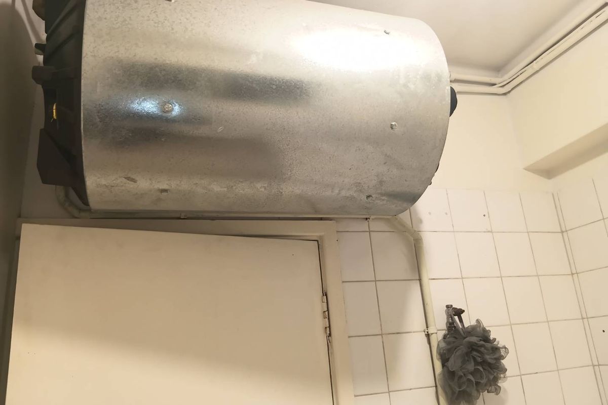 A bathroom interior featuring an exposed wall-mounted electric water heater and basic white wall tiling.