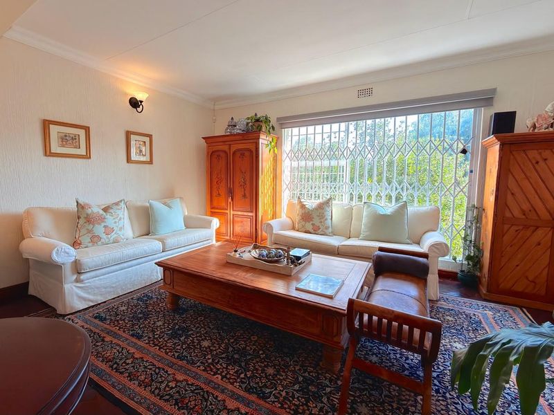 A comfortable living room featuring timber flooring, decorative coving, and a large window fitted with a security gate for added protection.
