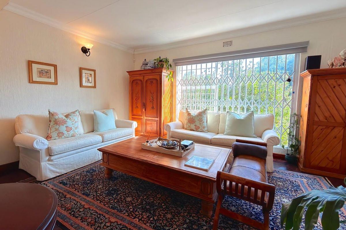 A comfortable living room featuring timber flooring, decorative coving, and a large window fitted with a security gate for added protection.