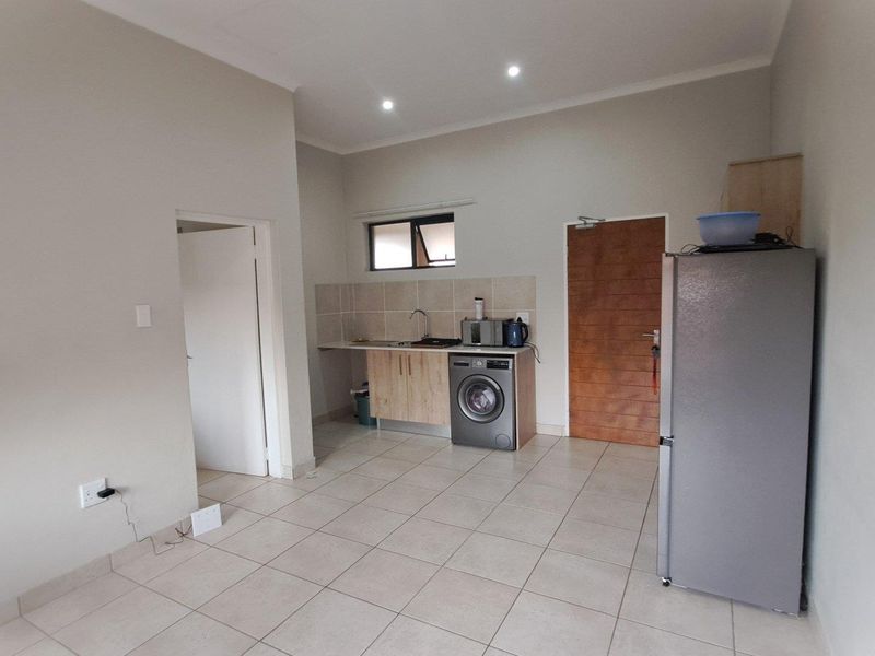 A functional kitchen area featuring tiled flooring, built-in cabinetry with a sink, and a tiled backsplash, offering a clean and practical layout.