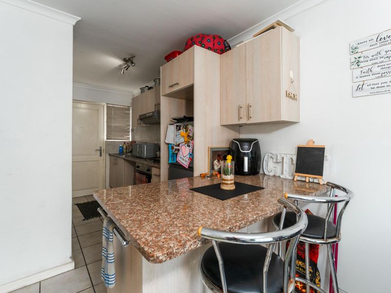 Compact kitchen featuring light wood-finish cabinetry, granite countertops, a breakfast bar, and tiled flooring, providing a functional and efficient cooking and dining space.
