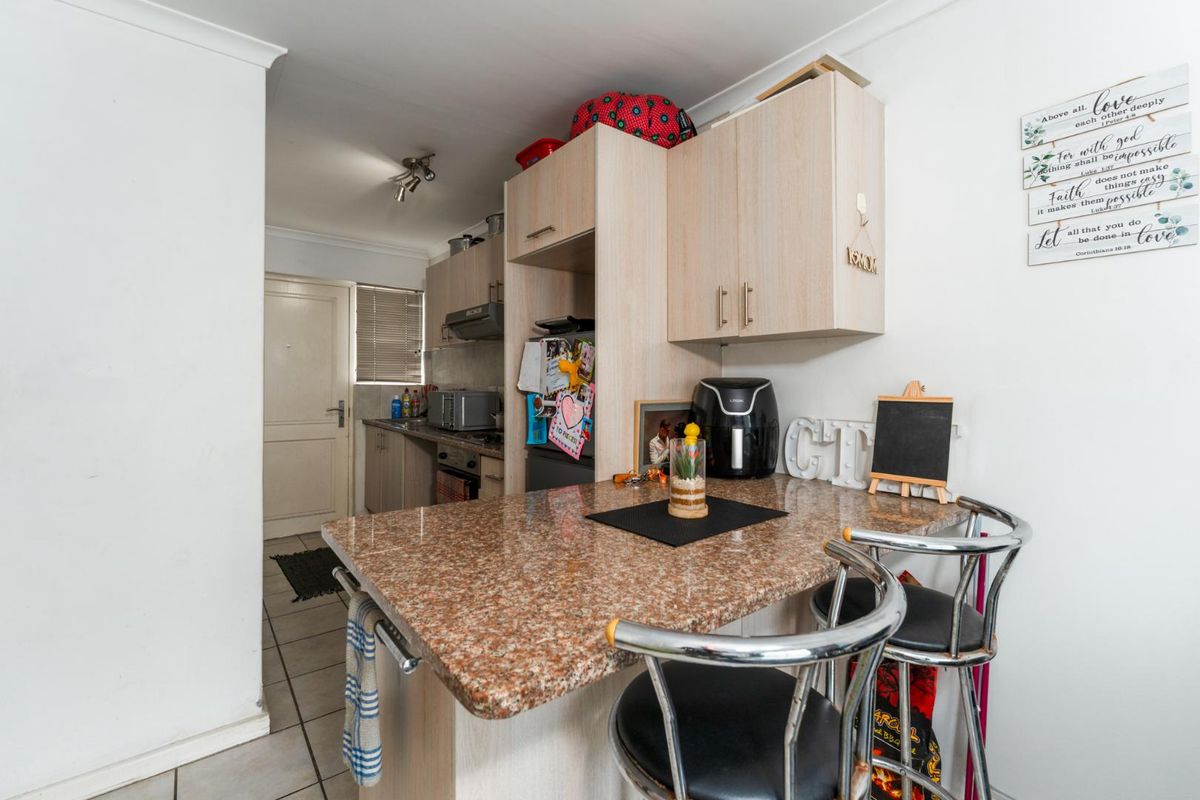 Compact kitchen featuring light wood-finish cabinetry, granite countertops, a breakfast bar, and tiled flooring, providing a functional and efficient cooking and dining space.