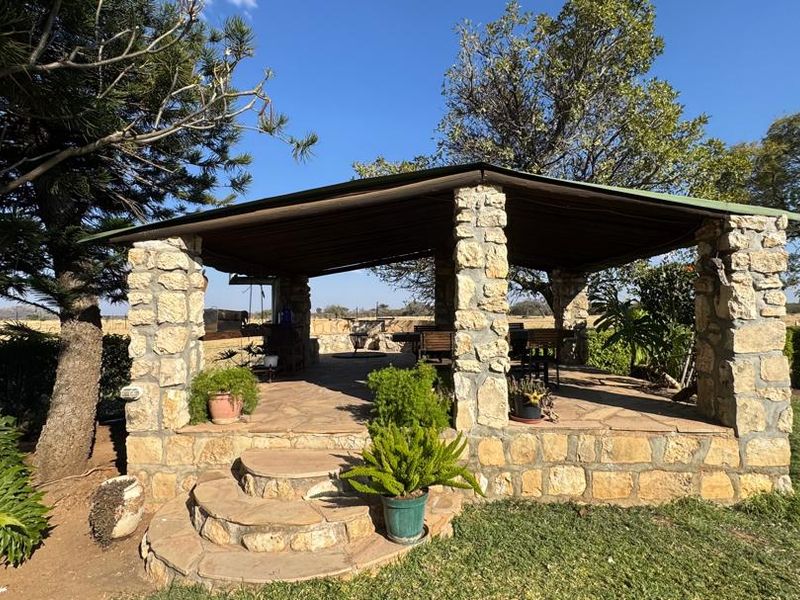 A charming outdoor stone-built patio area featuring rustic masonry pillars, stone flooring, and steps, set within a spacious garden environment.