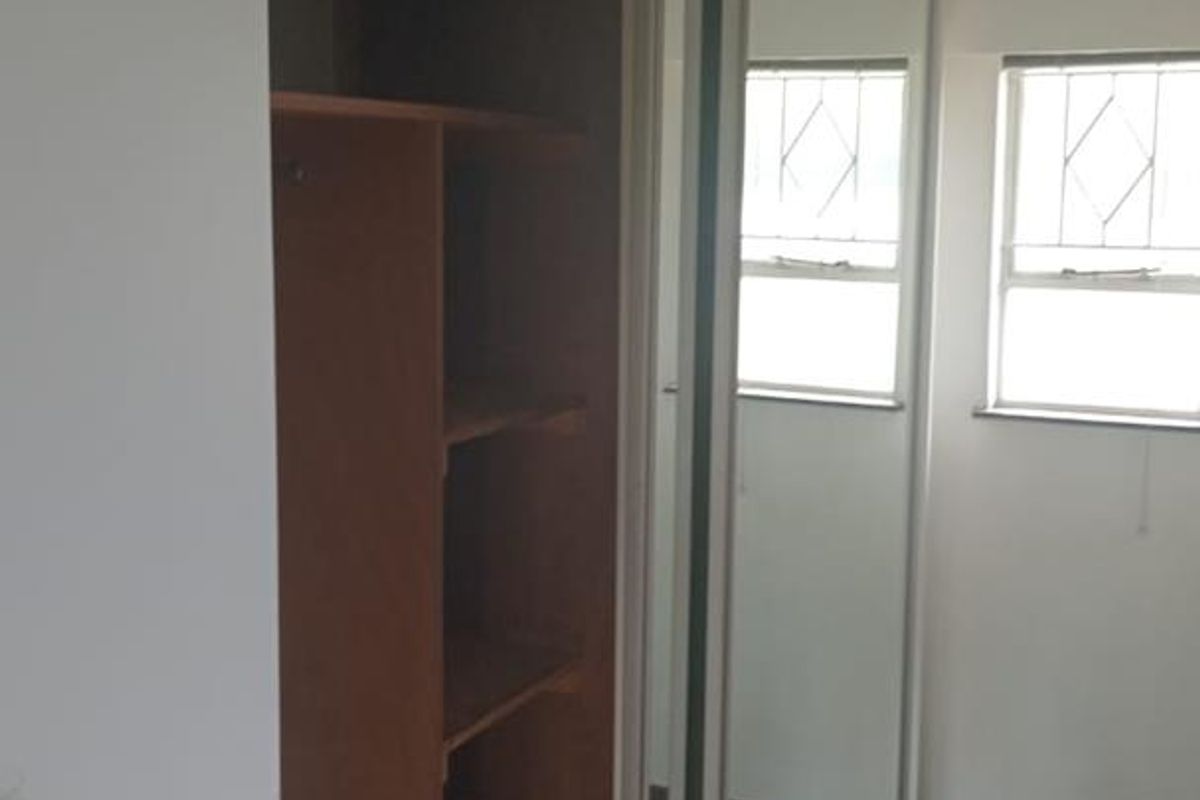 A bedroom featuring built-in mirrored sliding wardrobes with internal shelving and dual windows providing natural light.