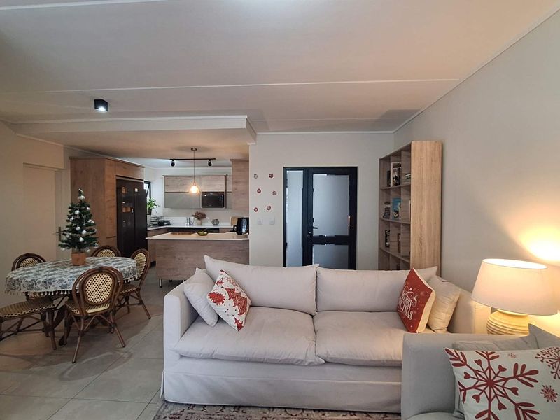 An open-plan living and dining area featuring a modern kitchen with an island, tiled floors, and a distinctive white brick feature wall.