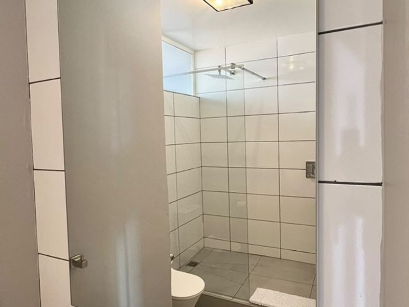 Modern bathroom featuring a walk-in shower with glass screen, wall-mounted mirror, basin with chrome faucet, and contemporary tiled finishes.