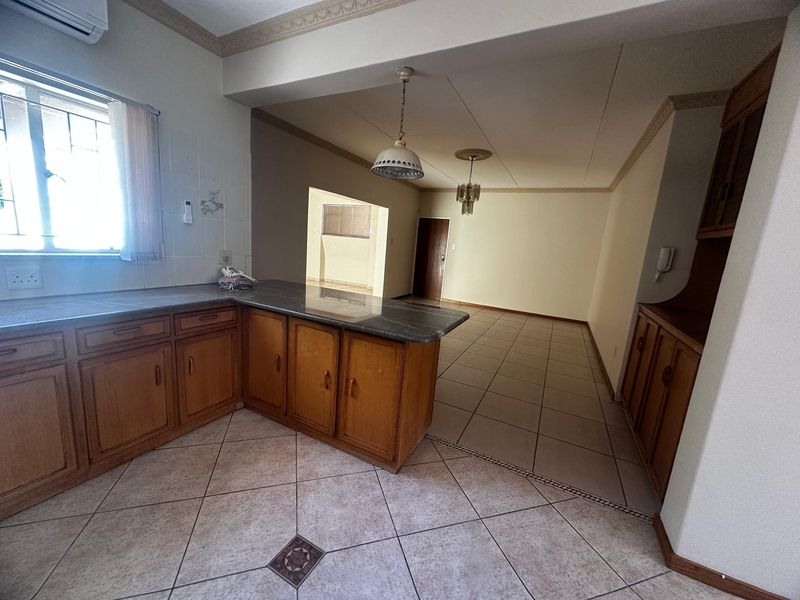 Open-plan kitchen and living area featuring wooden cabinetry, stone countertops, tiled flooring, and decorative ceiling cornices in a spacious, neutral layout.
