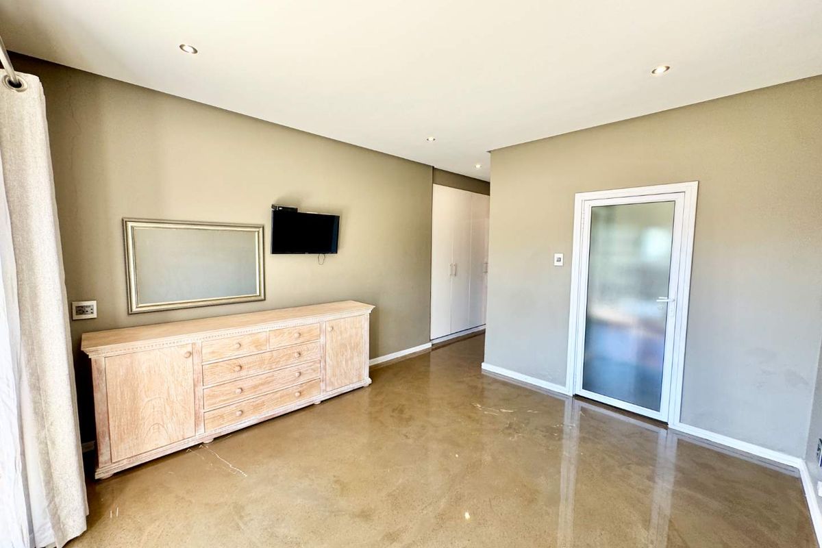 A spacious bedroom featuring polished concrete flooring, built-in cupboards, and a glass-panelled door leading to an adjoining area.